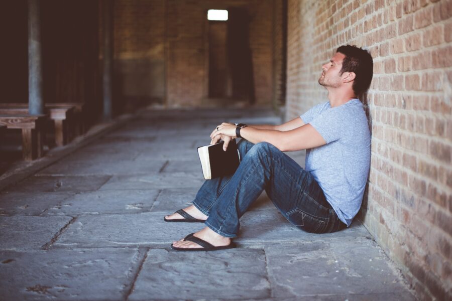 A man sitting against a brick wall holding a Bible, reflecting on Bible verses for overcoming anxiety and fear.