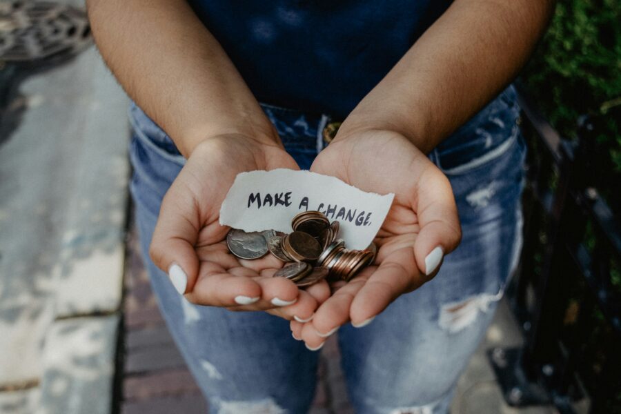 Hands holding loose coins and a note reading 'Make a Change,' representing the heart of generous living and the impact of selfless giving.