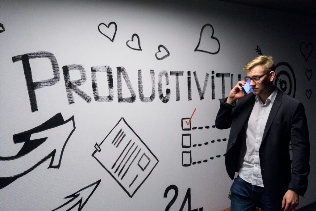 man in a business suit holding a phone, standing in front of a wall with the word 'Productivity' and illustrations of checkboxes and arrows, symbolizing the connection between humility, serving others, and redefining true success.