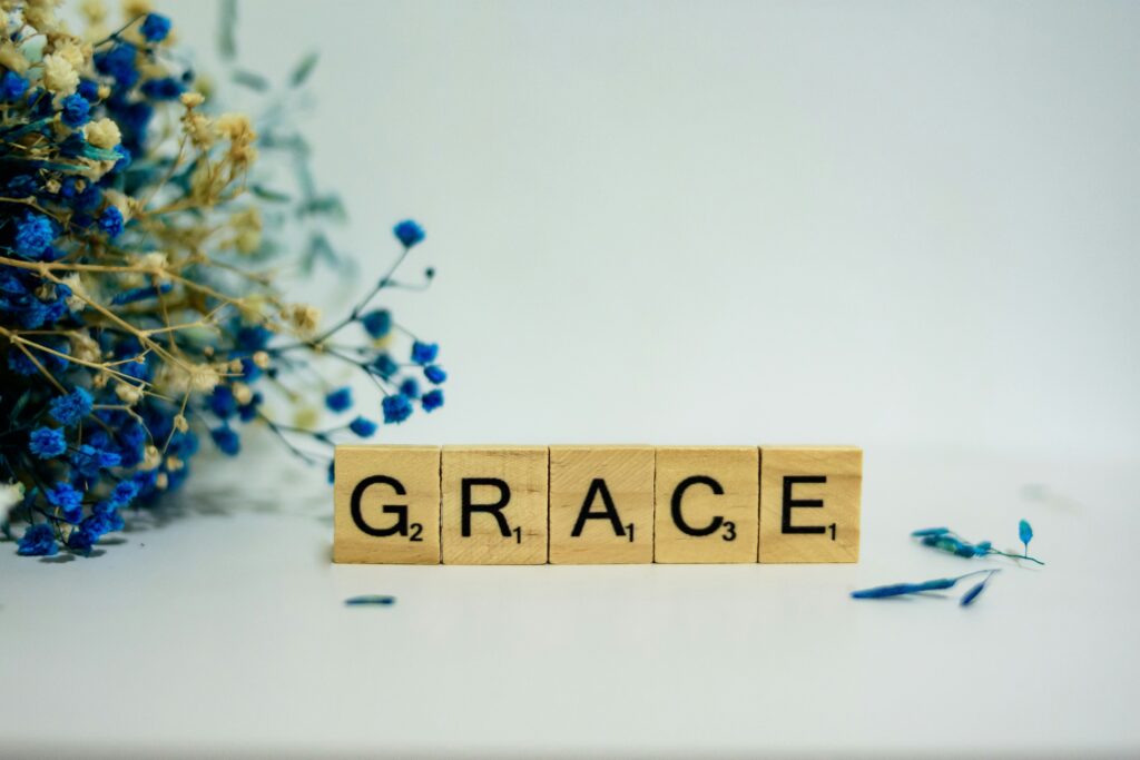 Wooden letter tiles spelling "GRACE" on a white surface, with delicate blue and white flowers in the background.