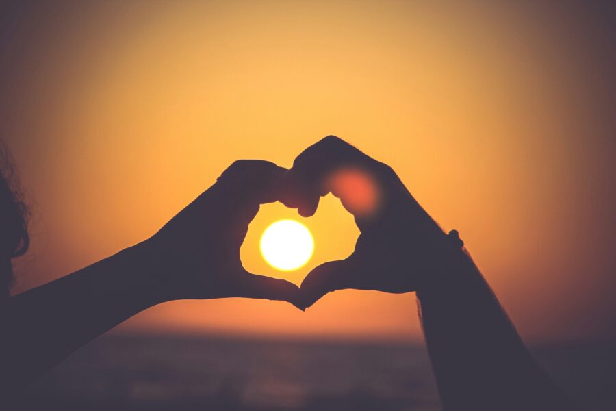 Better Together: Silhouette of two hands making a heart shape around the sun against a sunset sky.