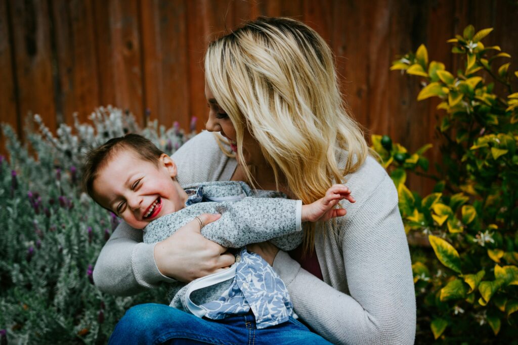 Mother hugging laughing son outdoors, celebrating love and connection on Mother’s Day.